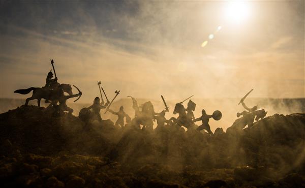 صحنه نبرد قرون وسطی با سواره نظام و پیاده نظام سیلوئت های فیگورها به عنوان اشیاء جداگانه جنگ بین جنگجویان در پس زمینه مه آلود غروب آفتاب تمرکز انتخابی