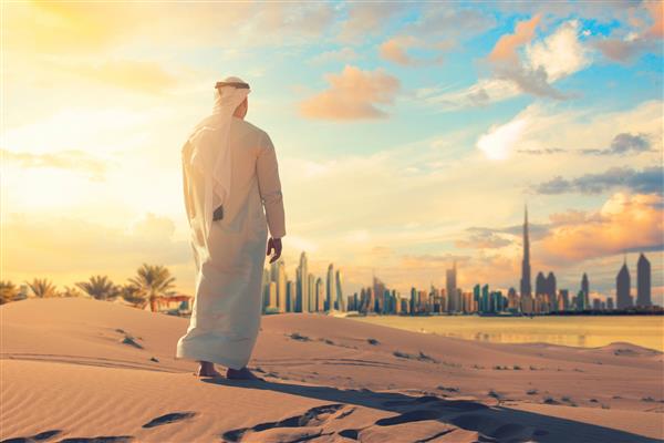 مرد عرب ایستاده جلوی افق دبی در صحرای امارات