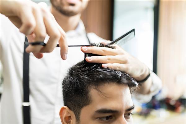دستان آرایشگر با استفاده از قیچی برای کوتاه کردن موهای مشتری در سالن