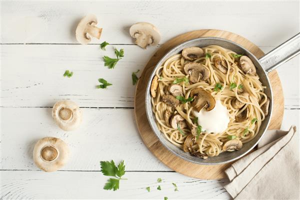 ماکارونی اسپاگتی قارچ و سس خامه ای در زمینه سفید نمای بالا ماکارونی خانگی ایتالیایی با قارچ شامپینیون در تابه پخت و پز