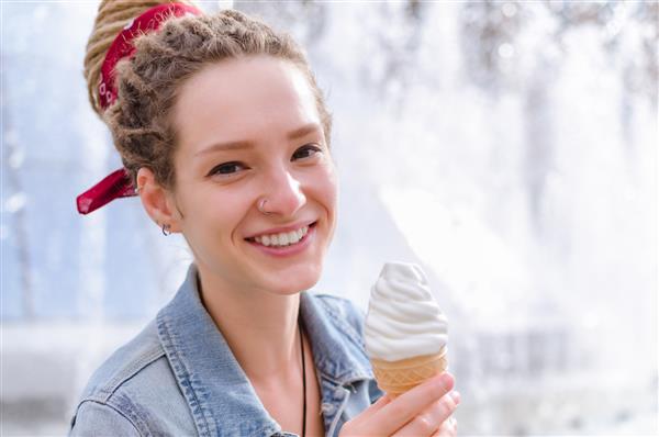 زن جوان با ژاکت جین با قیفی بستنی در نزدیکی فواره در کیف نشسته است