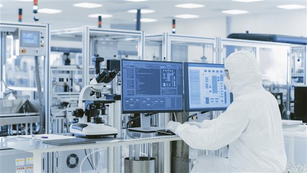 در آزمایشگاه از روی شانه دانشمندی با لباس های محافظ که در حال انجام تحقیق بر روی رایانه شخصی است کارخانه مدرن تولید نیمه هادی ها و اقلام دارویی