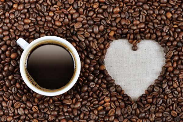 شکل قلب ساخته شده از دانه های قهوه با یک فنجان قهوه روی پارچه کتان