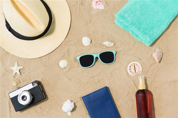 مفهوم تعطیلات سفر و گردشگری - دوربین قدیمی پاسپورت کلاه و عینک آفتابی روی شن و ماسه ساحل