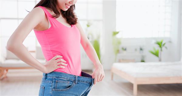 زن آسیایی زیبایی شلوار جین گشاد را با مفهوم کاهش وزن نشان می دهد