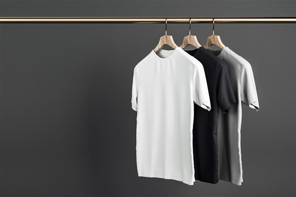 پیراهن های خاکستری سفید و مشکی خالی روی چوب لباسی پس زمینه دیوار بتنی طراحی فروشگاه و مفهوم سبک ماکت رندر سه بعدی