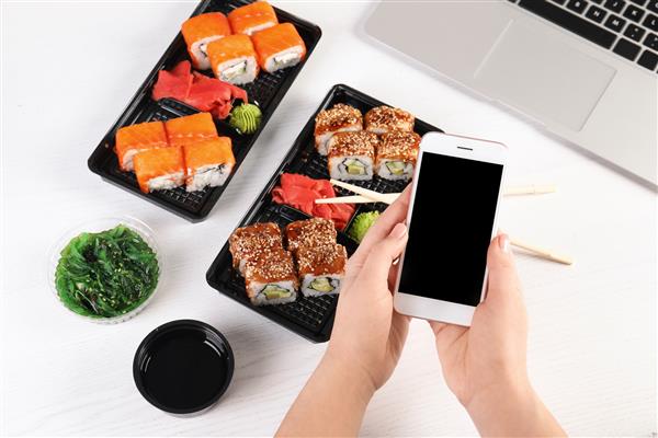 زنی با تلفن همراه و سوشی روی میز فضایی برای متن تحویل غذا