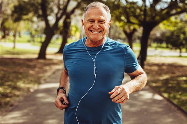پرتره مرد سالخورده ای با لباس تناسب اندام که در پارکی می دود مردی خندان از نزدیک در حالی که با استفاده از گوشی به موسیقی گوش می دهد می دود
