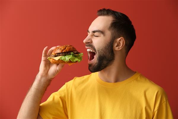 مردی در حال خوردن برگر خوشمزه در پس زمینه رنگی