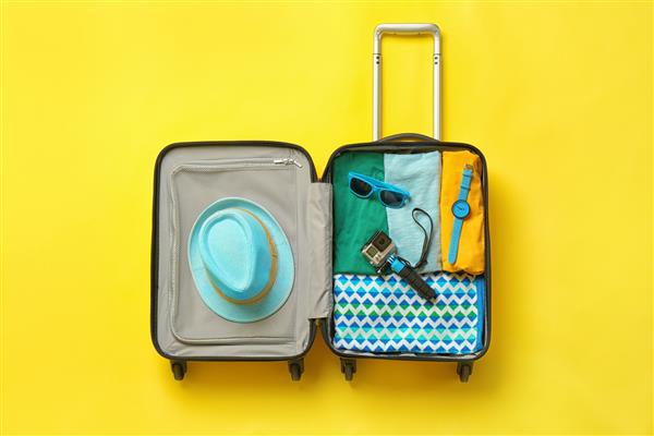چمدان باز با لباس های تابستانی و لوازم جانبی در پس زمینه رنگی نمای بالا