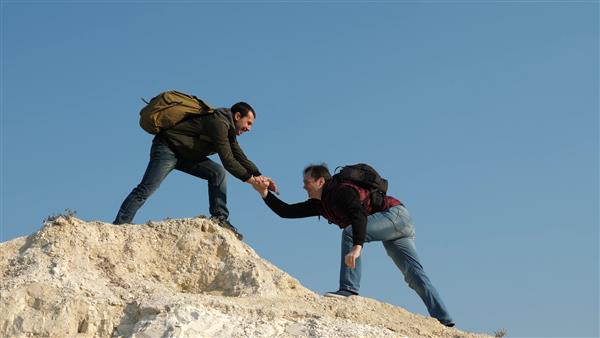 دو کوهنورد یکی پس از دیگری بر روی صخره های سفید صعود می کنند کار گروهی افراد تجاری گردشگران با بالا رفتن از بالای تپه به یکدیگر دست می دهند تیم مسافران مرد به پیروزی و موفقیت می رود