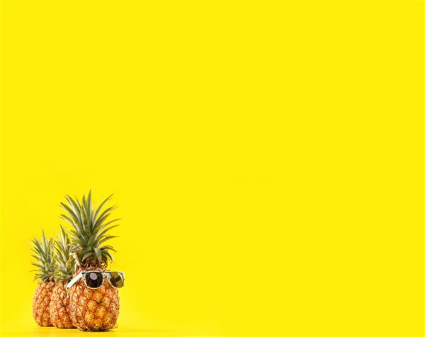 آناناس خلاق با عینک آفتابی و صدف جدا شده روی پس‌زمینه زرد الگوی طراحی ایده ساحل در تعطیلات تابستانی فضای کپی از نزدیک