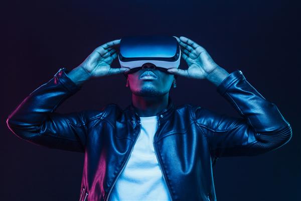 مرد آفریقایی آمریکایی با عینک واقعیت مجازی در حال تماشای ویدیوی 360 درجه با هدست واقعیت مجازی جدا شده روی پس‌زمینه سیاه
