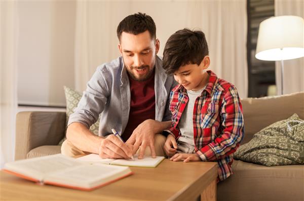 آموزش خانواده و مفهوم تکلیف - پدر و پسر شاد با نوشتن کتاب در دفترچه در خانه