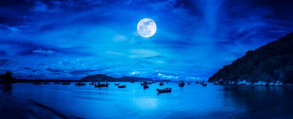 چشم انداز زیبای طبیعت پانوراما ساحل کنار دریا با کوه ها و ماه کامل در شب بسیاری از قایق های ماهیگیری شناور در خلیج دریا در جنوب تایلند ماه گرفته شده با دوربین من