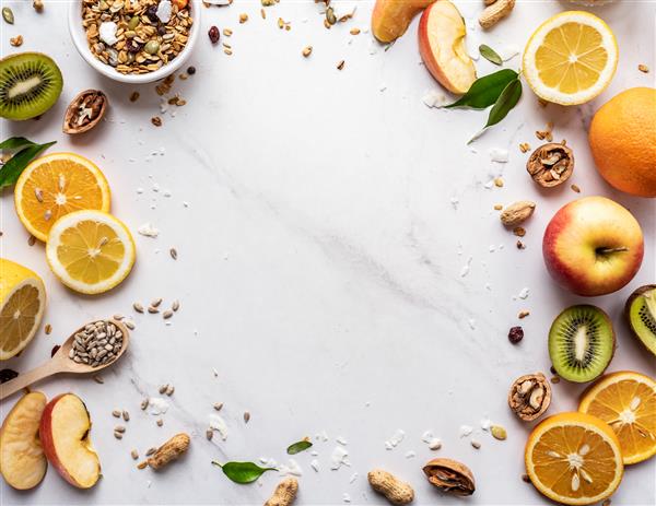 مفهوم تغذیه صبحانه وگان غذای سالم میوه های تازه تابستانی آجیل دانه های گرانولا در پس زمینه سفید سوپر غذای ارگانیک روی میز رژیم سم زدایی برای مراقبت های بهداشتی نمای نزدیک از بالا فضای کپی