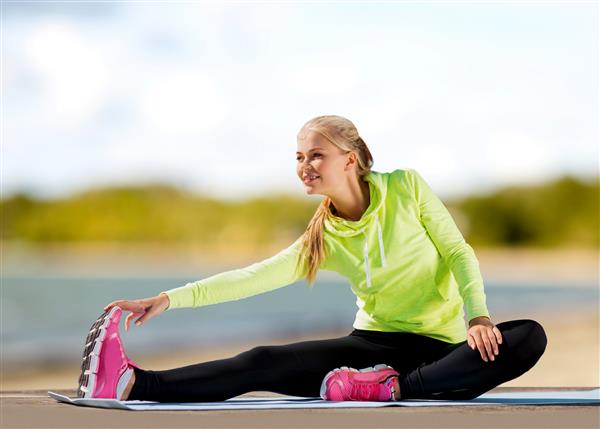 مفهوم تناسب اندام ورزش و سبک زندگی سالم - پاهای کشیده زن روی تشک ورزشی در پس زمینه تابستانی ساحل