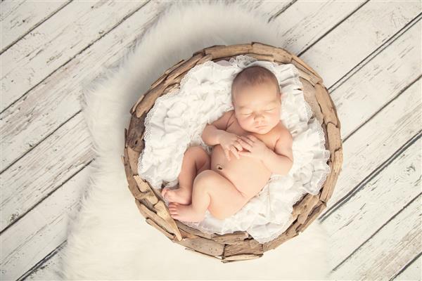 نوزاد دختری که در سبد روی زمین و خز چوبی سفید می خوابد