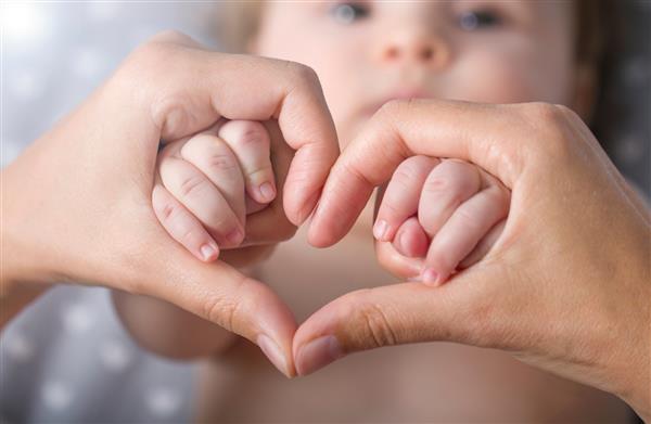نوزاد تازه متولد شده ای که دست های مادر را به شکل قلب گرفته است دست نوزاد نزدیک در انگشت مادر