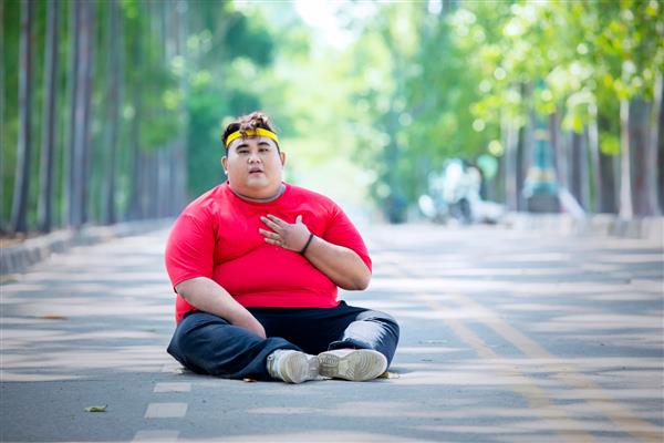 تصویر مرد جوان چاق که پس از دویدن در حالی که در پارک نشسته بود قلبش درد می کند