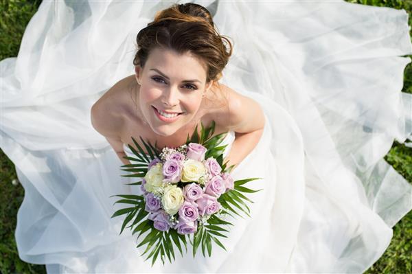 پرتره با نمای بالا از عروس خوشبخت زیبا که روی چمن نشسته است