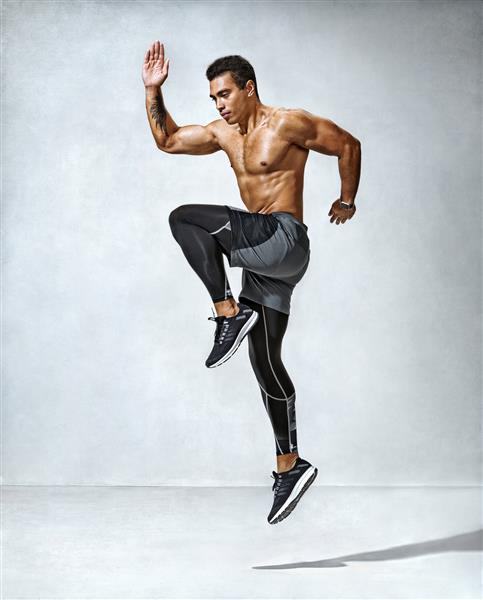 مرد ورزشکار در حال پریدن عکس مرد فعال با نیم تنه برهنه در پس زمینه خاکستری حرکت پویا نمای کنار ورزش و سبک زندگی سالم