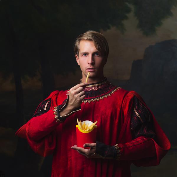 مرد خوش تیپ با دوبل قرمز سلطنتی در حال خوردن سیب زمینی سرخ کرده جعبه سرخ شده سیب زمینی سرخ شده دوئت خنده دار سبک قرون وسطایی و ویژگی های مدرن مفهوم