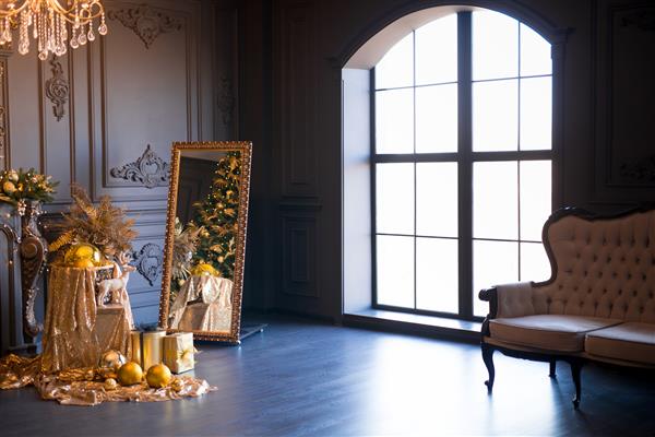 فضای داخلی اتاق نشیمن لوکس مدرن با شومینه مبل راحتی و لوستر تزئین شده با درخت کریسمس طلایی و هدایا