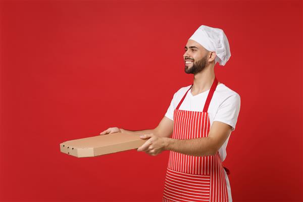 مرد خندان سرآشپز مرد ریشدار آشپز یا نانوا با پیش بند راه راه کلاه سرآشپزها جدا شده در پس زمینه قرمز مفهوم آشپزی غذا ماکت کردن فضای کپی پیتزای ایتالیایی را در جعبه مقوایی تخت نگه دارید