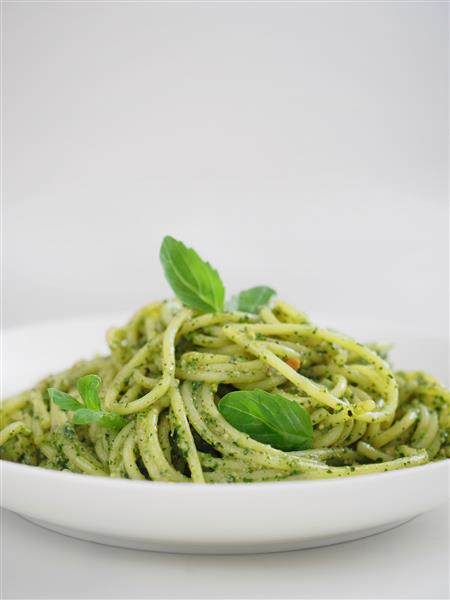 پاستا پستو یک پاستا معروف ایتالیایی است سس پستو وگان پیچیده شده در اسپاگتی با برگ ریحان طعم منحصر به فرد با طراوت سالم پس زمینه سفید