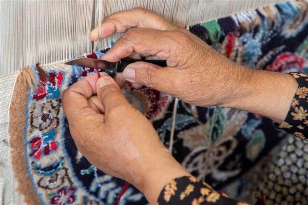 دست زن در حال بریدن نخ در قالیچه ایران