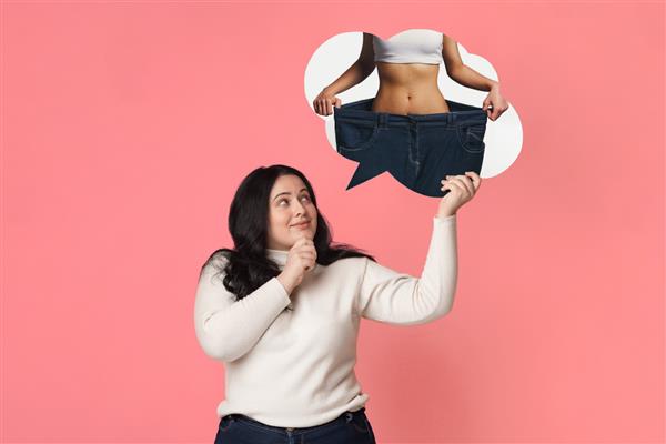 مفهوم کاهش وزن زن چاق که رویای بدن لاغری را در سر می پروراند هیکل اسپرت رویایی خود را در حباب گفتار پس زمینه صورتی در دست گرفته و به آن نگاه می کند