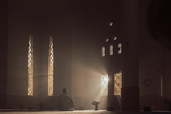 مردی در مسجد قرآن می خواند عرب با لباس سفید کندور لباس عربی در فضای باز مسجد قرآن شب خوانی قرآن رمضان اسلام دین اسلام