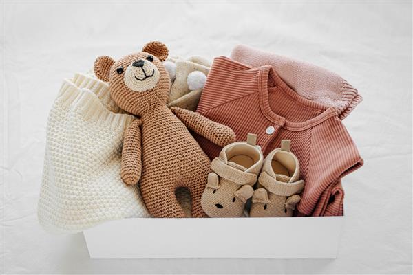 جعبه با وسایل و لوازم کودک برای نوزاد روی تخت جعبه هدیه با پتو بافتنی لباس جوراب کفش و اسباب بازی مفهوم حمام نوزاد تخت خوابیده نمای بالا