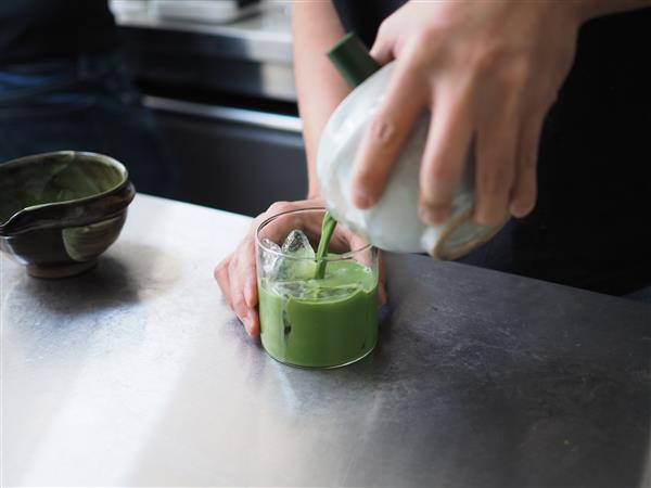 ماچا چای سبز - باریستا با ابزار سنتی ژاپنی ماچا ماچا را روی یک لیوان یخ می‌ریزد تمرکز انتخابی