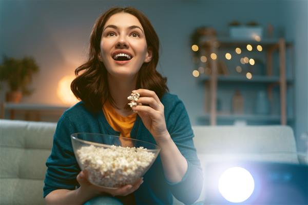 زن جوان در حال تماشای پروژکتور تلویزیون فیلم با پاپ کورن در شب دختری که در خانه وقت می گذراند