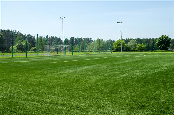 زمین فوتبال با چمن مصنوعی سبز و دروازه فوتبال در پس زمینه