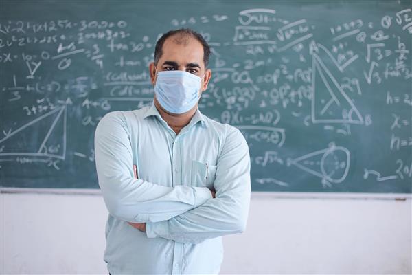 پرتره معلم مردی که ماسک به تن دارد و در مقابل تخته سیاه در حال تدریس ریاضیات در کلاس درس ایستاده است مدرسه پس از قرنطینه به دلیل همه‌گیری کووید-19 بازگشایی می‌شود سویه جدید ویروس کرونا موارد omicron