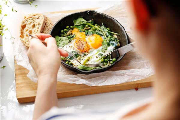 تخم مرغ سرخ شده روی اسفناج و نخود سبز صبحانه رژیمی زن در حال خوردن صبحانه است