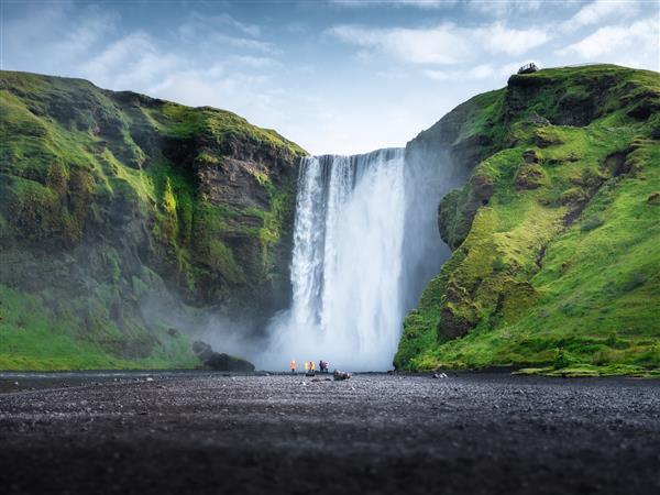 آبشار اسکوگافوس ایسلند دره کوه و آسمان صاف چشم انداز طبیعی در فصل تابستان طبیعت ایسلندی گروهی از مردم در نزدیکی آبشار بزرگ تصویر سفر
