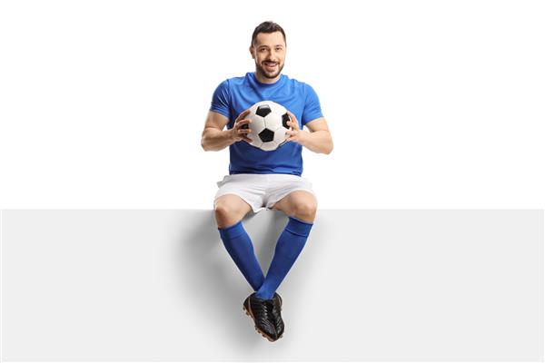 فوتبالیستی که روی یک پانل خالی نشسته و یک توپ فوتبال جدا شده روی پس‌زمینه سفید را در دست دارد