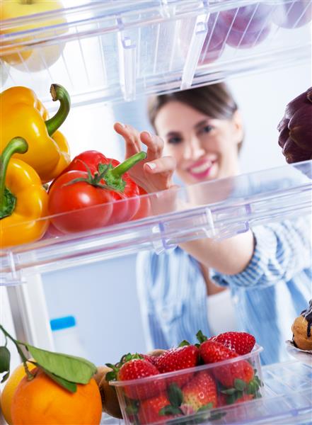 زن جوانی که سبزیجات سالم تازه را از یخچال می گیرد