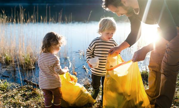 پدری با بچه‌های کوچک که زباله‌ها را در طبیعت جمع‌آوری می‌کنند مفهوم پلاگ کردن
