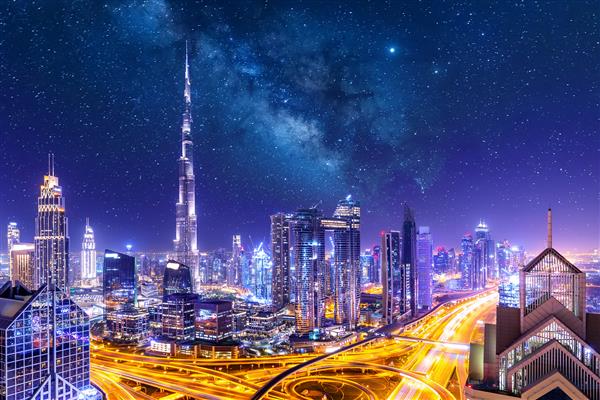 منظره شهری شگفت انگیز با آسمان خراش های نورانی مرکز شهر دبی در شب با ستاره ها و راه شیری امارات متحده عربی