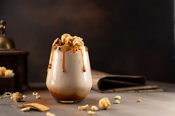 میلک شیک شیرین با شربت کارامل لیکور خامه پاپ کورن کاراملی و پودر شکلات در زمینه قهوه ای با آسیاب قهوه وینتیج دستی