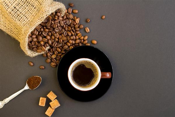 نمای بالای قهوه سیاه در فنجان قهوه‌ای و دانه‌های قهوه در پس‌زمینه تیره