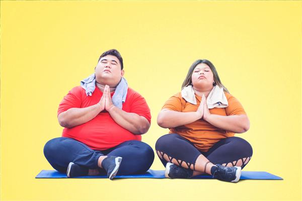 زوج چاق جوانی که لباس ورزشی می پوشند و در حال انجام تمرینات یوگا با هم در حال مدیتیشن در استودیو با زمینه زرد