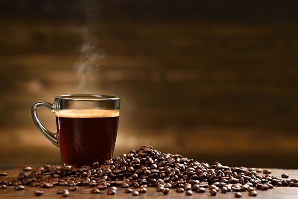فنجان قهوه با دود و دانه های قهوه در زمینه چوبی قدیمی