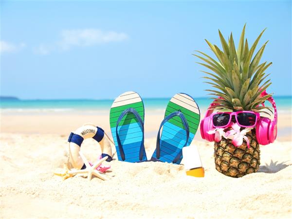 مهمانی تابستانی آناناس با عینک آفتابی و گوش دادن به موسیقی با ضد آفتاب و صندل در ساحل و پس زمینه آسمان آبی مد استوایی مد تابستان در مفهوم تعطیلات