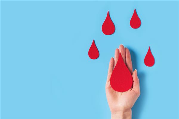 مفهوم روز جهانی هموفیلی با نماد قطره خون قرمز و دست روی پس‌زمینه آبی فضای کپی نمای بالا